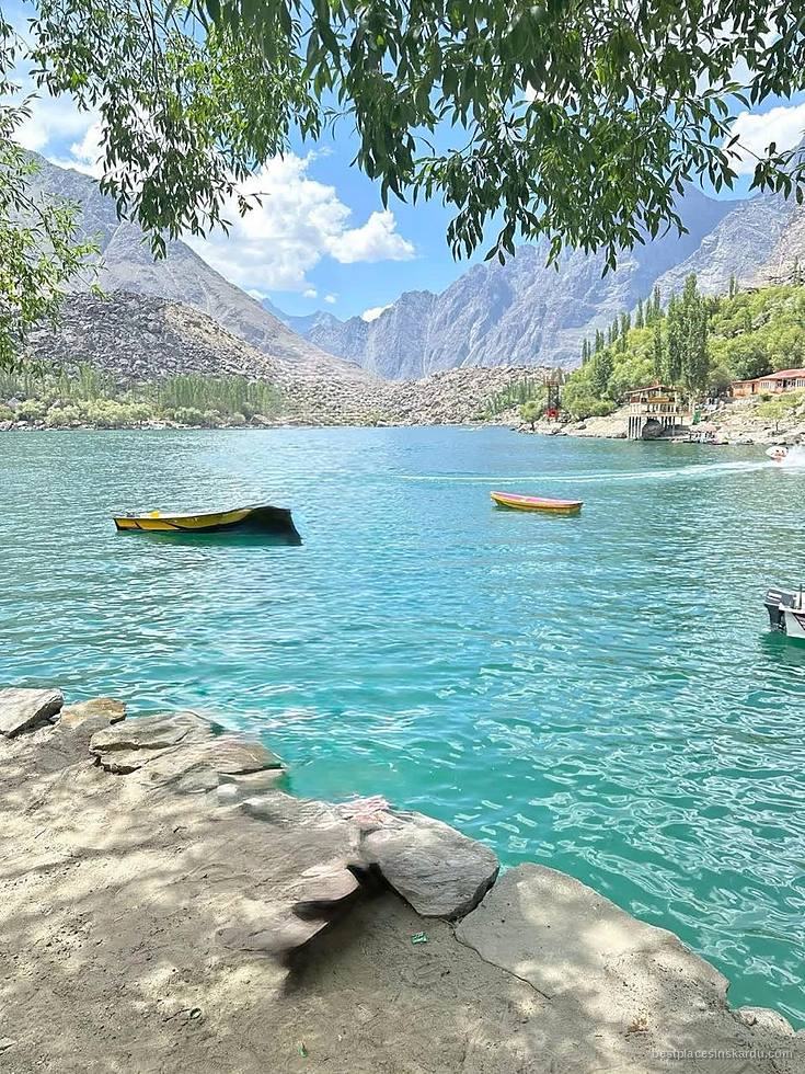 Turquoise water of Upper Kachura Lake with wooden boats, framed by willow trees near Skardu